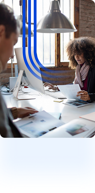 A computer monitor and a large industrial pendant light are visible. In the foreground, the shoulder of another person is seen. Three bold, blue curved lines overlay the center of the image, swooping down from the top