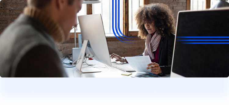 A wide horizontal photograph of two people working in a bright, brick-walled office. In the center. The image is stylized with blue graphic lines: three vertical lines curving toward the center and three horizontal lines on the far right.